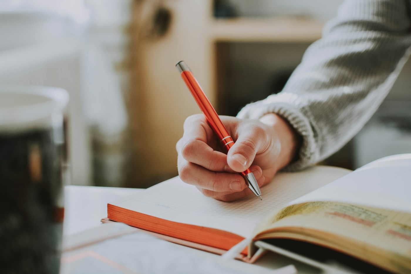 A hand writing in an open notebook with a red pencil