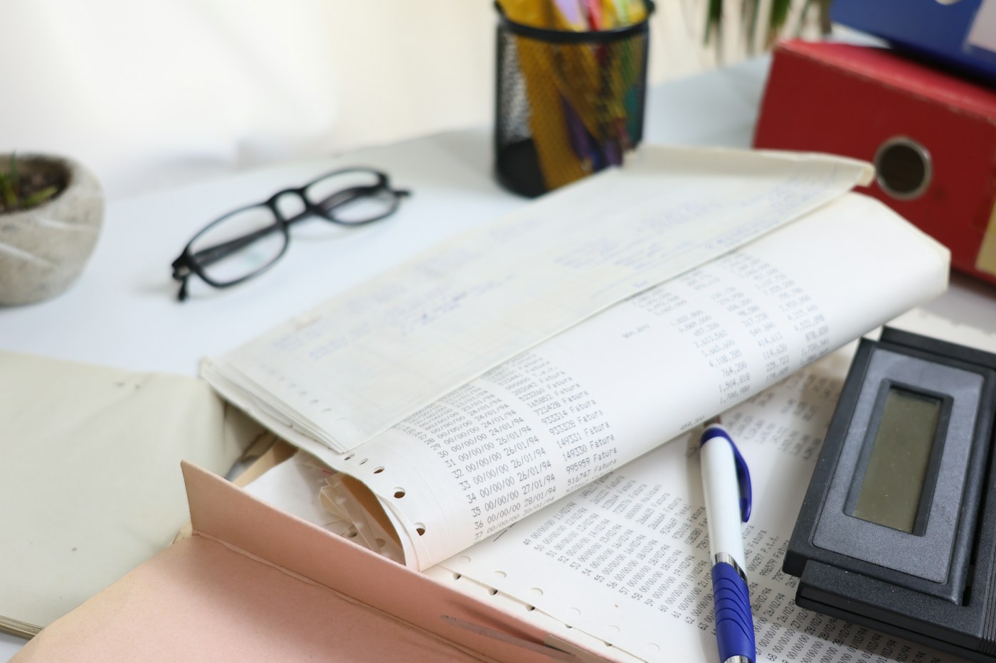 Calculator, glasses, pen and pages of figures on a desk